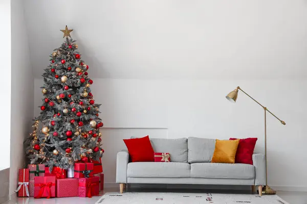 クリスマスツリーの下に灰色のソファーとギフトボックスが付いたお祝いのリビングルームのインテリア — ストック写真