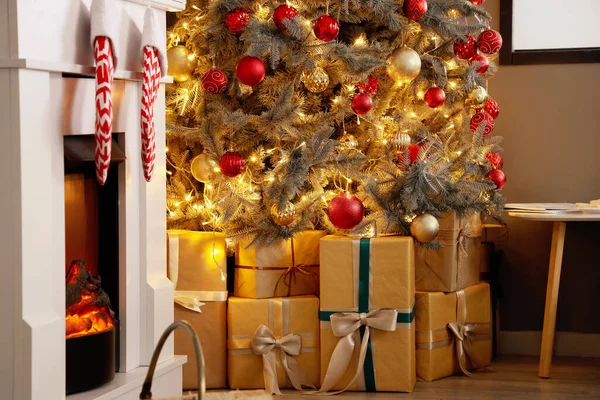 クリスマスツリーの下に暖炉とギフトボックス付きのお祝いのリビングルームのインテリア — ストック写真