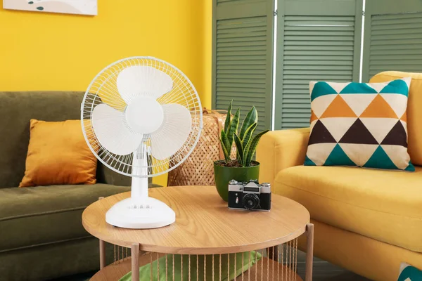 Modern electric fan and photo camera on coffee table in interior of living room