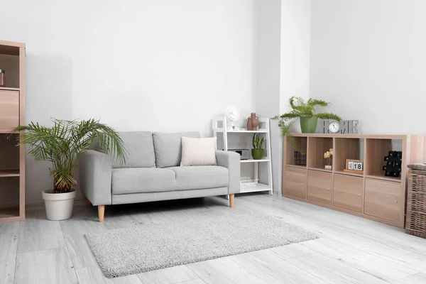 Interior of light living room with grey sofa and modern fan on shelving unit