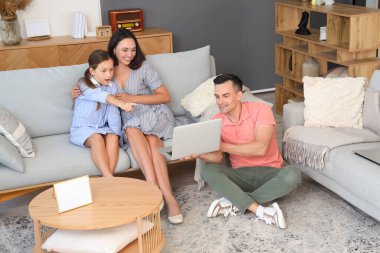 Oturma odasında dizüstü bilgisayarı olan mutlu bir aile.