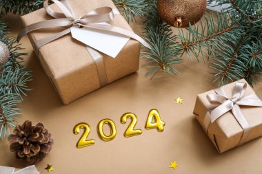 Noel ağacı dallarıyla ve kahverengi arka planda hediye kutularıyla 2024 'ü düşün.