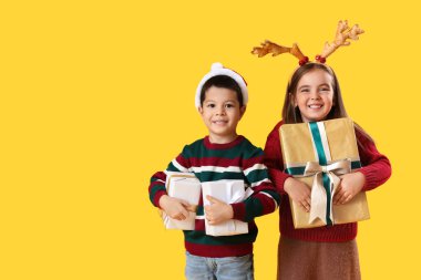 Sarı arka planda Noel hediyeleri olan şirin çocuklar.