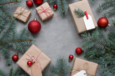 Noel ağacı dallarından yapılmış bir çerçeve. Topları ve gri arka planda hediye kutuları var.