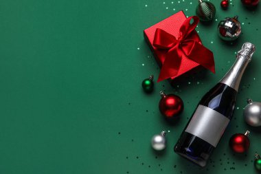 Bir şişe şampanya, hediye kutusu ve yeşil arka planda Noel süslemeleri.