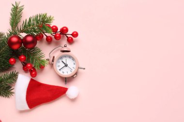 Alarm saati ve Noel Baba şapkası, pembe arka planda topları olan Noel ağacı dalları.