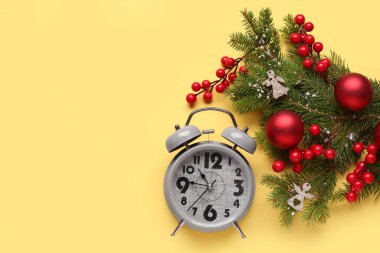 Alarm saati ve sarı arka planda topları olan Noel ağacı dalları