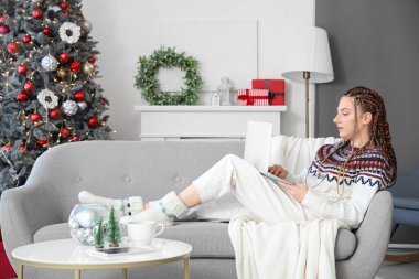 Noel arifesinde evde dizüstü bilgisayar kullanan genç bir kadın.