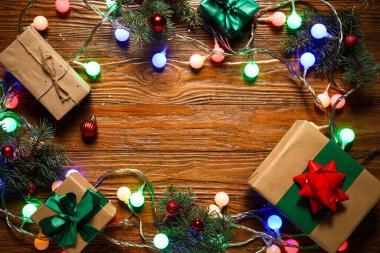 Ahşap arka planda güzel Noel ışıklarından, toplardan ve hediye kutularından yapılmış çerçeve