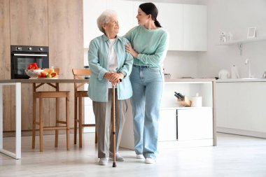 Bastonlu son sınıf öğrencisi kadın ve kızı mutfakta.