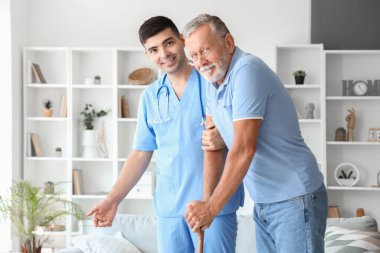 Erkek hemşire, kıdemli bir adamın evde yürümesine yardım ediyor.