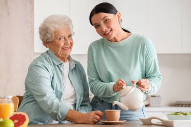 Genç bir kadın mutfakta annesi için sıcak çay dolduruyor.