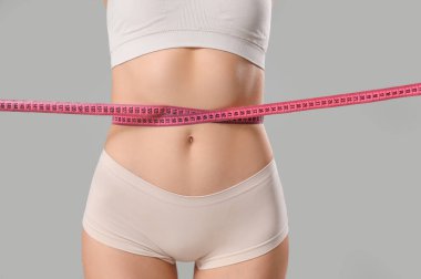 Gri arka planda belini ölçen güzel bir genç kadın, yakın plan. Kilo verme konsepti