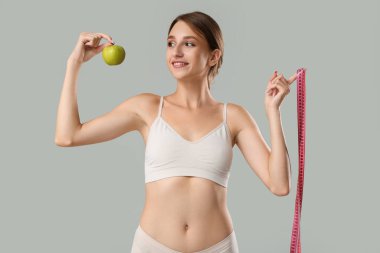 Elmalı ve gri arka planda şeritli güzel bir genç kadın. Kilo verme konsepti