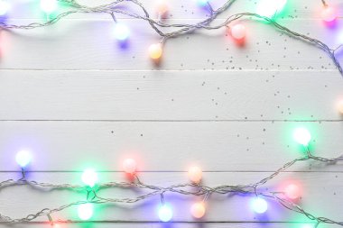 Beyaz ahşap arka planda parlayan Noel ışıklarından yapılmış çerçeve