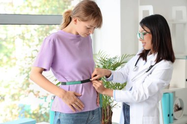 Kadın Asyalı beslenme uzmanı ofisteki hastanın belini ölçüyor.