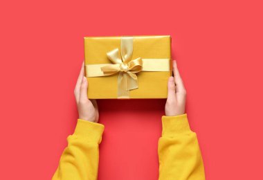 Kırmızı arka planda Noel hediyesi olan kadın eller, yakın plan.