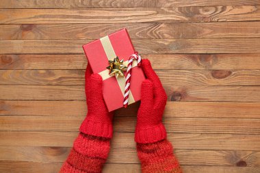 Tahta arka planda Noel hediyesi olan sıcak eldivenli kadın eller, yakın plan.