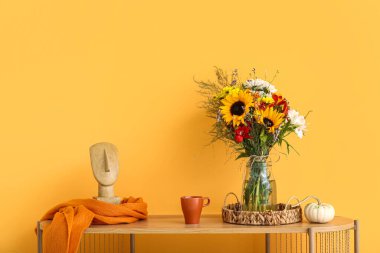 Sonbahar çiçekleri, balkabağı ve turuncu duvarın yanında dekoru olan ahşap raf ünitesi.