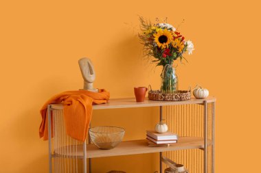 Sonbahar çiçekleri, balkabakları ve turuncu duvarın yanında dekoru olan ahşap raf ünitesi.