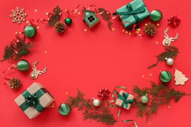 Güzel Noel süsleri ve kırmızı arka planda hediye kutuları olan kozalaklı dallardan yapılmış bir çerçeve.