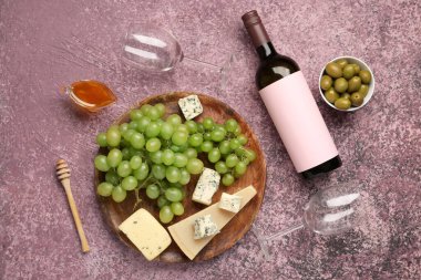 Mor zemin üzerinde üzüm, peynir ve bal olan bardaklar ve bir şişe şarap.