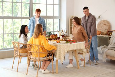 Bir grup genç arkadaş Şükran Günü 'nde şenlik masasında yemek yiyor.