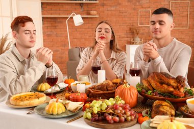 Şükran Günü 'nde şenlik masasında dua eden bir grup genç arkadaş.
