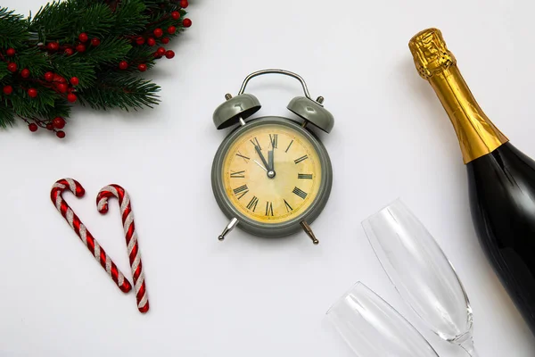 Alarm clock with Christmas tree branches and bottle of champagne on white background