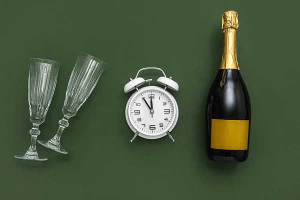Alarm clock with champagne and glasses on green background