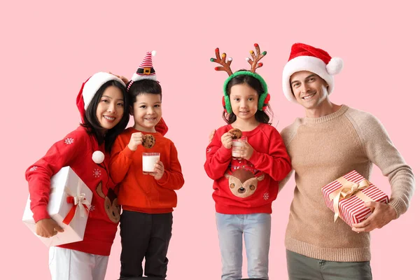 Happy family with Christmas presents, milk and cookies on pink background