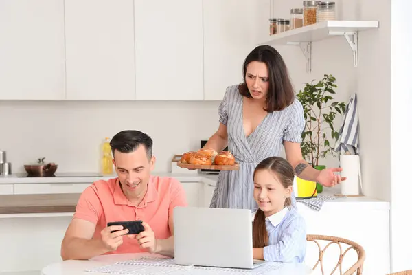 Frustrated mother concerned about family involved with gadgets at table in kitchen