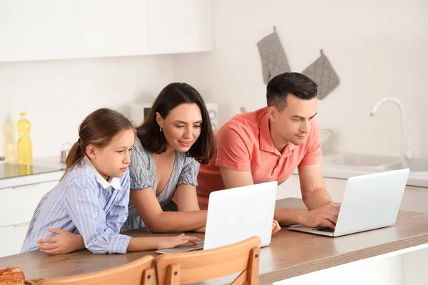Family with laptops resting at table in kitchen