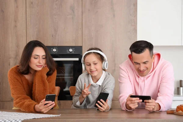 Happy family with mobile phones resting at table in kitchen