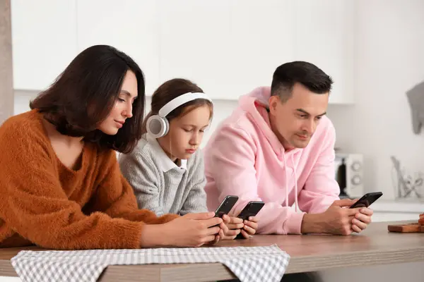Family involved with mobile phones at table in kitchen