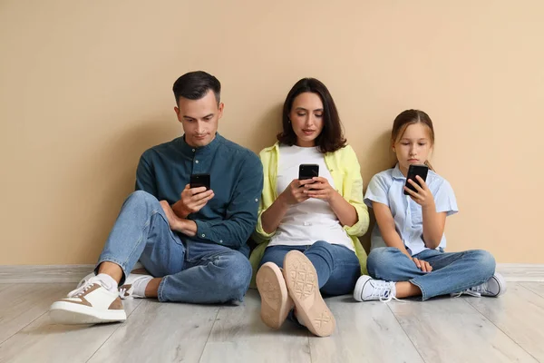 Family involved with mobile phones sitting near beige wall