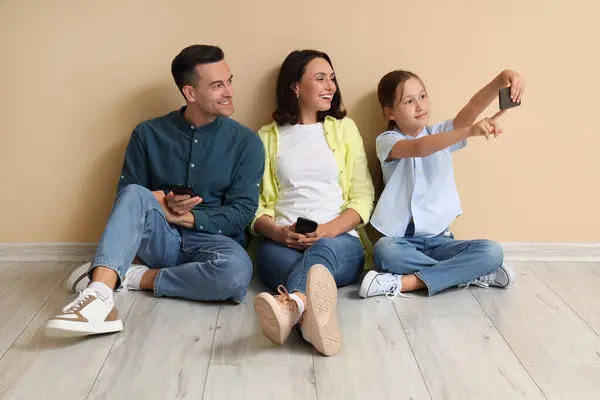 Счастливая Семья Мобильными Телефонами Сидит Бежевой Стены Делает Селфи — стоковое фото