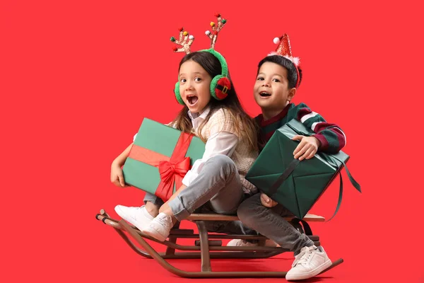 Emotionale Kleine Kinder Mit Weihnachtsgeschenken Und Schlitten Auf Rotem Hintergrund — Stockfoto