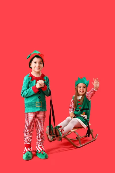 Niedliche Kleine Kinder Als Elfen Mit Schlitten Auf Rotem Hintergrund — Stockfoto
