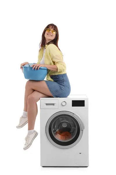 Ung Kvinna Med Tvättkorg Sitter Tvättmaskin Mot Vit Bakgrund — Stockfoto