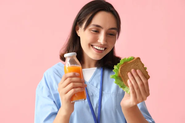Jonge Vrouwelijke Arts Met Fles Sinaasappelsap Lekkere Sandwich Roze Achtergrond — Stockfoto