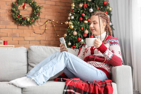 Noel arifesinde evde cep telefonu kullanan bir fincan kakaolu genç kadın.