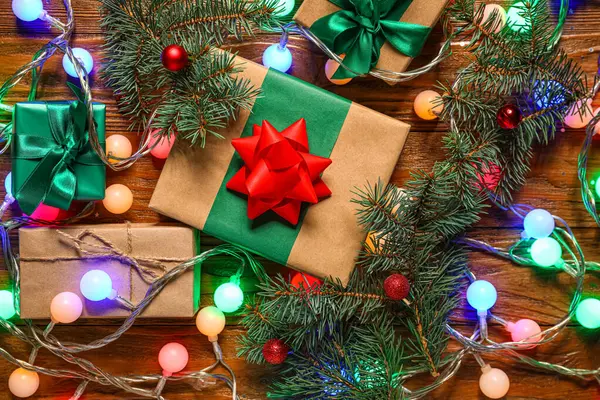 Güzel Noel ışıkları, köknar dalları, toplar ve tahta arka planda hediye kutuları.