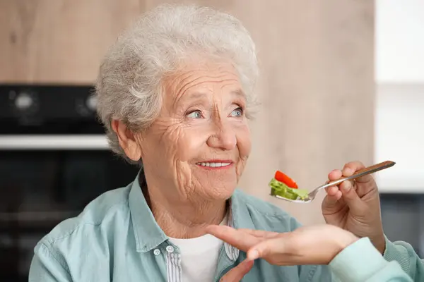 Senior woman with her daughter eating vegetable salad in kitchen, closeup