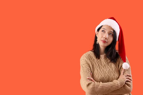 Kırmızı Arka Planda Noel Baba Şapkalı Düşünceli Güzel Asyalı Kadın — Stok fotoğraf