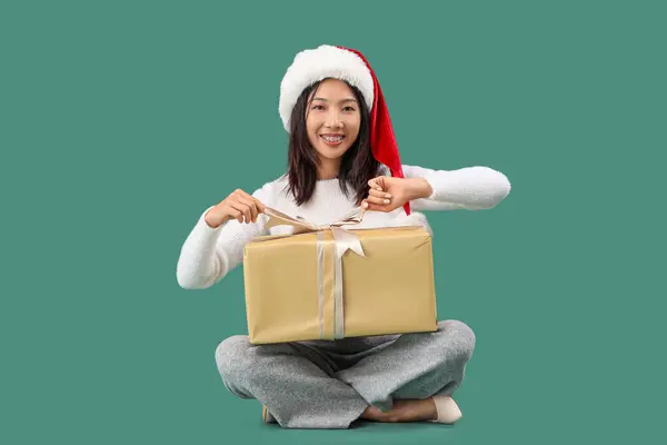 Молодая Красивая Азиатка Санта Шляпе Подарочной Коробкой Сидя Зеленом Фоне — стоковое фото