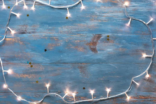 Mavi ahşap arka planda parlayan Noel ışıklarından yapılmış çerçeve