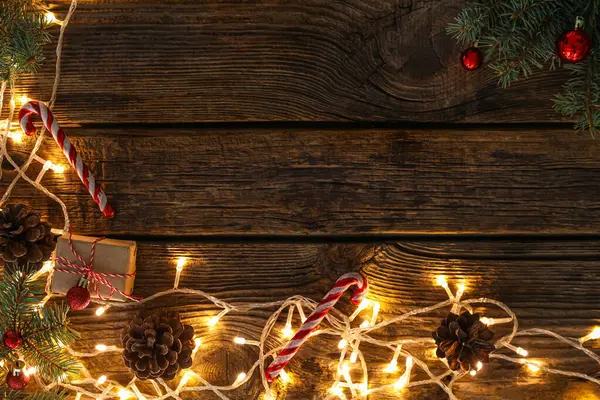 Noel hediyelerinden yapılmış çerçeve, köknar konileri ve ahşap arka planda parlayan ışıklar