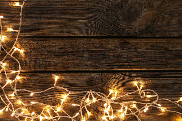 Frame made of glowing Christmas lights on wooden background