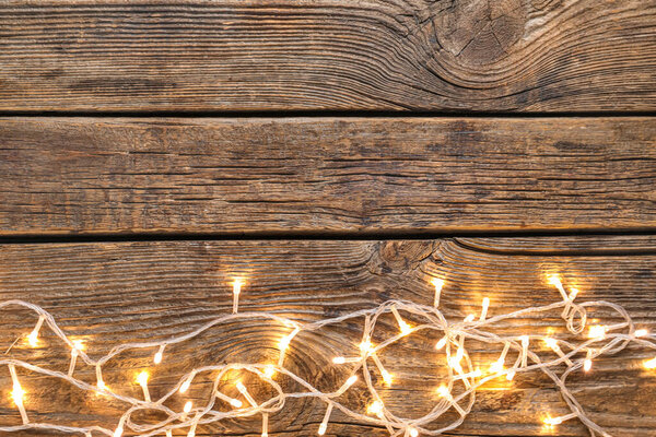 Glowing Christmas lights on wooden background
